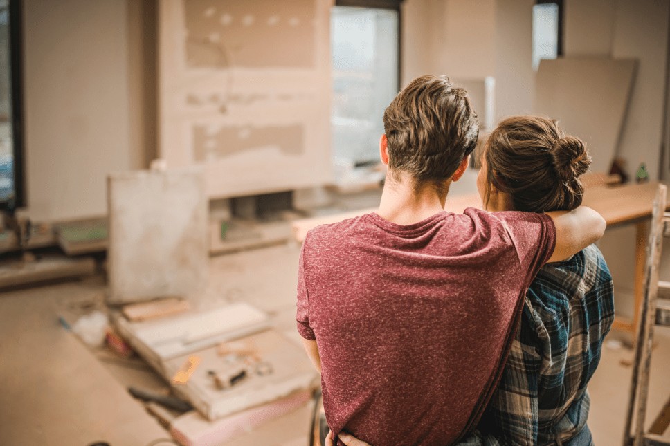 A man and woman embracing as they look into their living room that is being renovated and rebuilt.