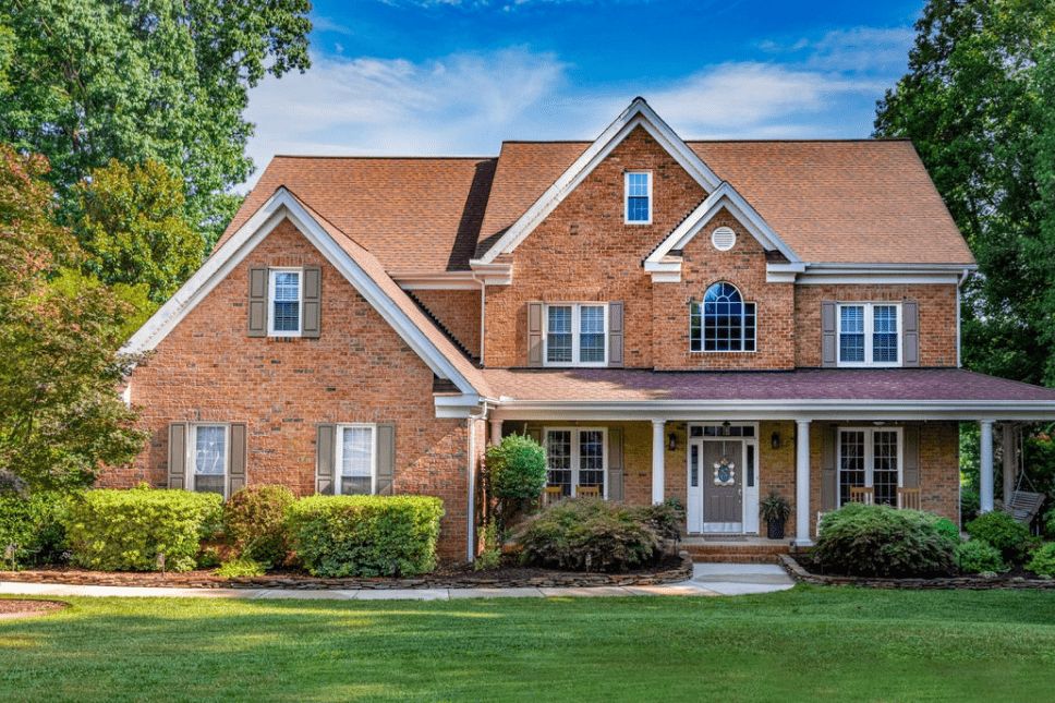 Brick home with white double-hung and picture windows with a well-kept yard and greenery shown.
