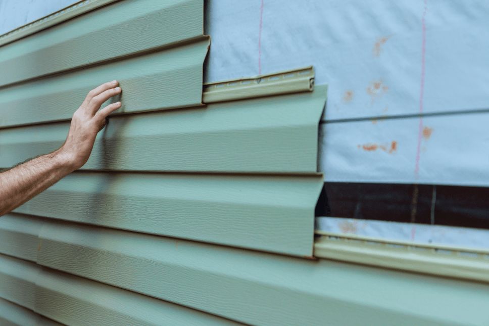 Person installing mint colored siding on a house.