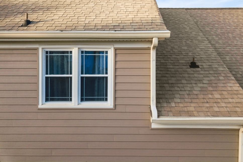 The second story of a home with tan siding and beige asphalt shingles.